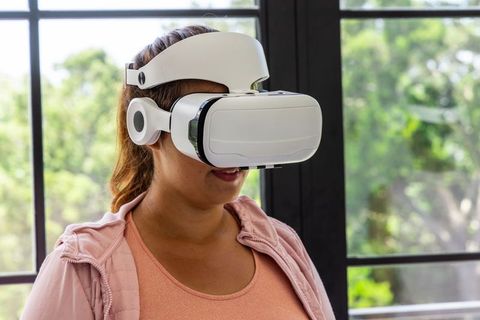 African american woman exploring virtual reality wearing vr headset and pink hoodie at home