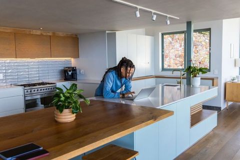 African american man working on laptop at kitchen island in modern sunlit home