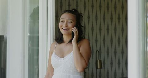 Smiling Woman Talking on Smartphone Steps Away from Window