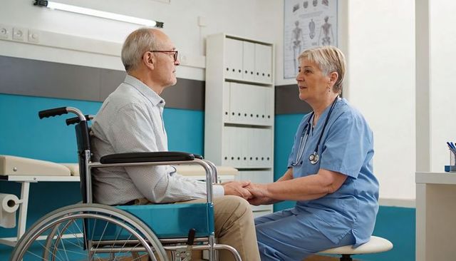 Nurse comforting senior man in wheelchair during outpatient consultation