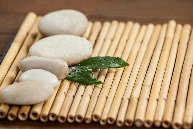 Two green leaves and four white stones on the bamboo mat  - Download Free Stock Photos Pikwizard.com