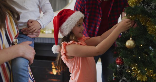 Family members decorating Christmas tree with ornaments and having fun together. Living room decorated with festive decorations including a fireplace in background. Perfect for Christmas ads, holiday promotions, and family celebration visuals.