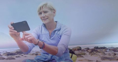 Senior woman taking selfie on rocky seaside, embracing relaxation