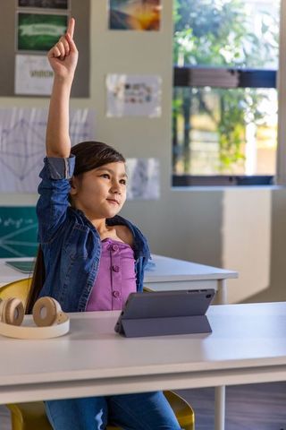 Asian schoolgirl raising hand while using tablet in classroom for interactive learning