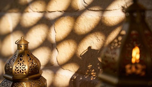 Brass moroccan lantern casting geometric shadows on stucco wall with warm candle glow