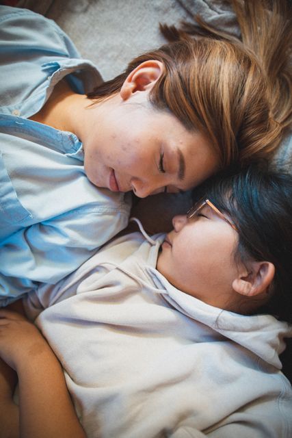 Asian mother and daughter lying asleep in bed facing each other, creating a peaceful and intimate family moment. Ideal for use in articles or advertisements related to family bonding, parenthood, quarantine life, and home comfort. Can also be used in content promoting mental health, relaxation, and the importance of rest.