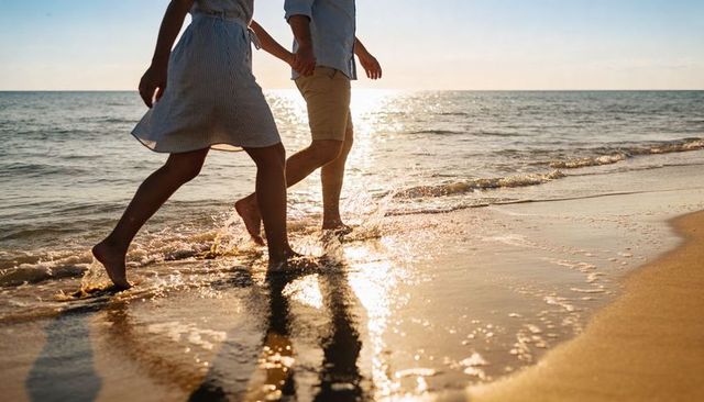 Couple walking barefoot along sunlit shoreline creating splashing footprints at sunset
