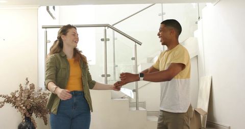 Young diverse couple laughing while unpacking in bright modern home with glass staircase