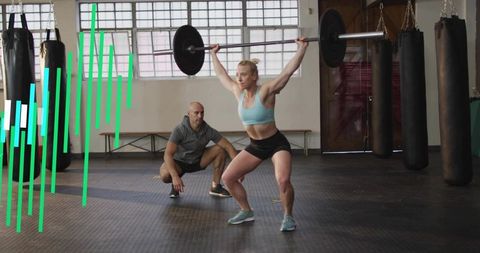 Female athlete performing overhead barbell squat while coach spotting in gym