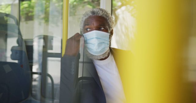 African american senior man wearing face mask talking on smartphone while sitting in the bus. hygiene and social distancing during coronavirus covid-19 pandemic.