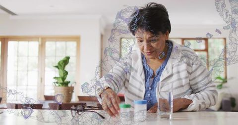 Senior woman reaching for medication bottles at kitchen table managing daily pill routine
