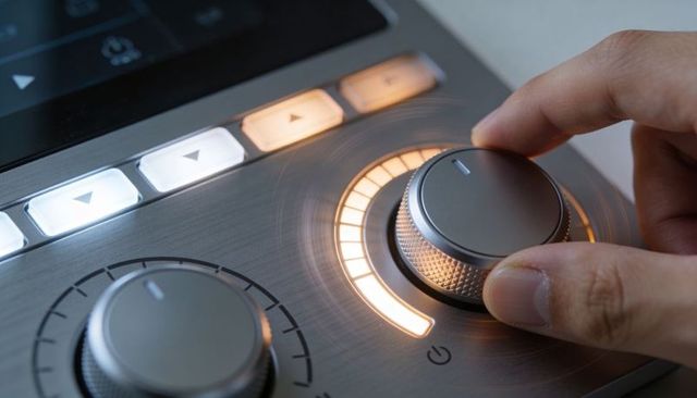 Engineer hand adjusting illuminated rotary knob on brushed-metal studio control mixer