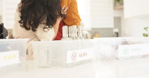 Hugging couple in kitchen embracing near labeled recycling bins glass plastic paper