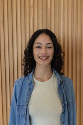 Asian woman smiling wearing denim overshirt and cream ribbed top against wood slat wall
