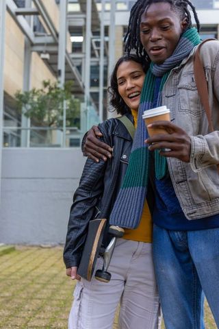 Campus couple walking with skateboard and coffee, urban casual lifestyle, candid moment