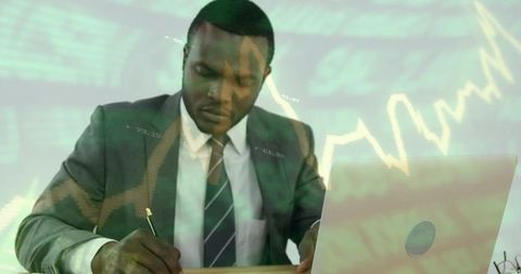 Businessman signing documents at desk with laptop and financial charts overlay