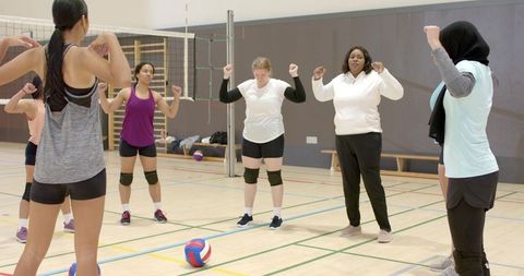 Multicultural women volleyball team practicing circle warmup in indoor gym
