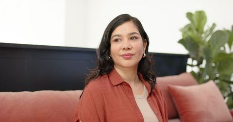 Serene woman sitting on coral-pink sofa wearing rust shirt in warm minimalist living room