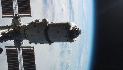 Orbiting cylindrical station module with solar arrays over earth horizon, antenna visible