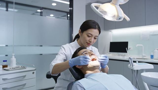 Female dentist examining patient in dental clinic under overhead light holding mirror and probe