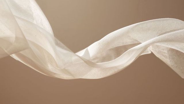 Floating sheer organza ribbon forming sinuous chiffon folds on warm beige background