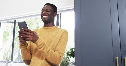 Relaxed Man Smiling with Smartphone in Modern Kitchen