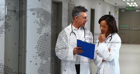 Medical team consulting in hospital corridor holding clipboard for clinical collaboration