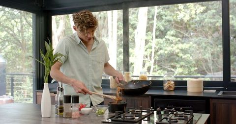 Young Man Cooking Asian Noodles in Modern Kitchen Setting