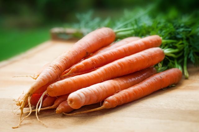 Fresh organic carrots lying on wooden surface with green tops intact. Perfect for promoting healthy eating, farm fresh products, and organic farming. Ideal for use in grocery store advertisements, recipe blogs, and health food campaigns.