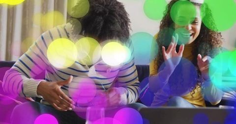 Friends cheering on sofa watching laptop with colorful bokeh celebration