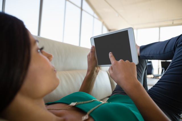 Young businesswoman using digital tablet while relaxing on sofa at office