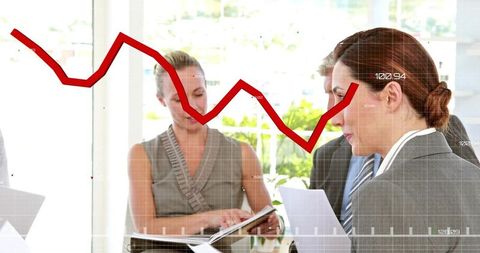 Business team reviewing reports with red declining line graph overlay in bright boardroom