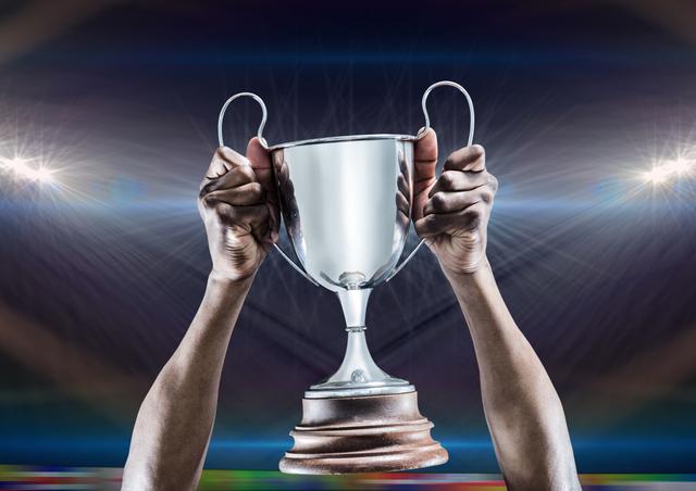 Close-up of athlete holding a silver trophy in a brightly lit stadium. The image conveys victory, achievement, and celebration. Perfect for use in sports marketing, motivational posters, or articles related to sports success and athletic achievement.