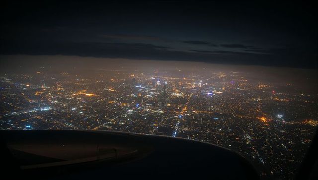 Night aerial view showing city lights below from aircraft window with wing silhouette