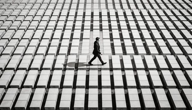 Solitary man walking across geometric concrete grid casting long shadow