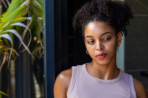 Thoughtful african american woman leaning in doorway wearing mauve top and hoop earrings