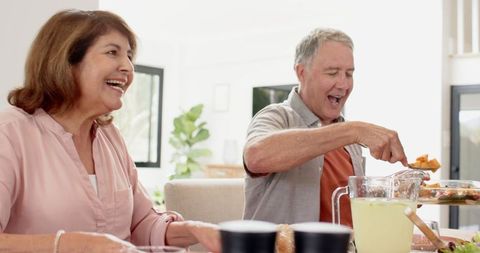 Joyful Senior Couple Sharing Meal at Dining Table in Modern Kitchen