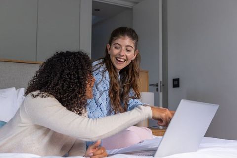 Diverse women collaborating on laptop in cozy bedroom