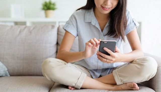 Relaxed woman scrolling smartphone on cozy neutral sofa, casual indoor lifestyle