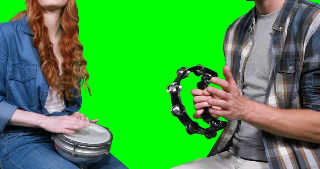 Mid section of musicians playing tambourine and drum against green screen