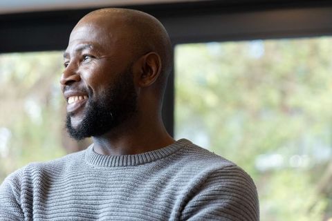 African american man smiling by window in cozy grey sweater serene natural light headshot