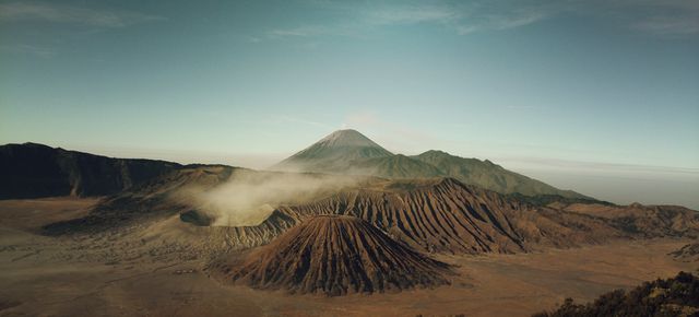 Panoramic view of Mount Bromo and surrounding volcanoes with morning mist and a clear sky, capturing the stunning and rugged landscape. Ideal for use in travel blogs, adventure websites, environmental campaigns, and tourism promotions to showcase natural beauty and geological wonder.