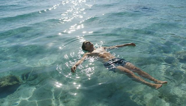 Adult man floating calmly on turquoise sea under sparkling sunlight for summer relaxation