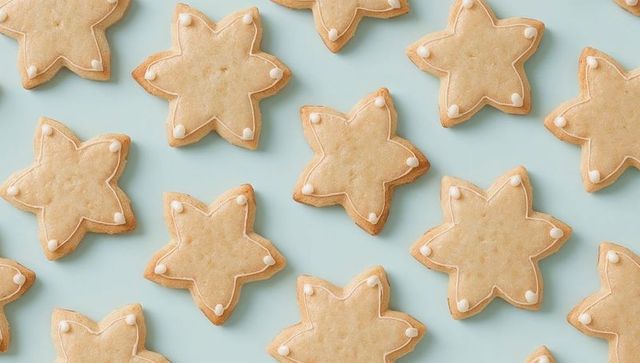 Arranging star-shaped shortbread cookies on pastel blue background with white icing dots