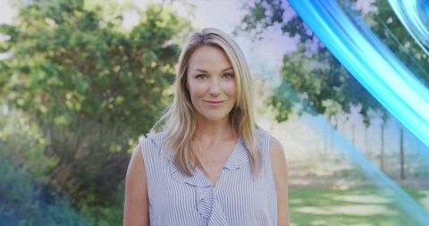 Smiling mature woman standing in sunny backyard garden wearing striped sleeveless blouse