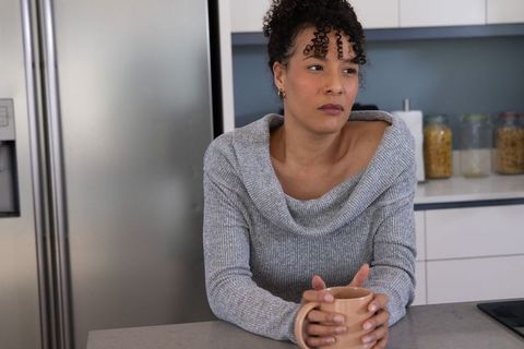 Contemplative african american woman holding mug in modern kitchen cozy off-shoulder sweater