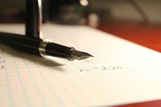 Close-up of a fountain pen resting on grid paper with handwritten mathematical equations. Useful for illustrating mathematical concepts, problem-solving, education, or stationary products. Ideal for use in educational materials, tutoring services, and stationary advertisements.