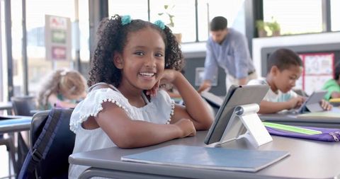 Smiling schoolgirl using tablet on stand in classroom for digital learning and edtech