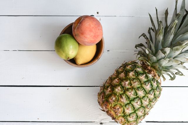 Fresh pineapple, peach, lime, and lemon on a white wooden table. Ideal for use in recipes, healthy living lifestyles, summer themes, and food blogs, emphasizing freshness and color.