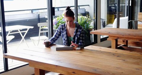 Businesswoman using tablet and drinking coffee in modern office cafeteria
